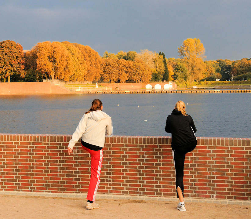 1366 Zwei Joggerinnen machen Lockerungsbungen an der Kaskade vom Stadtparksee im Stadtpark von Hamburg Winterhude -  Seeufer hohe Bume in Herbstfrbung .