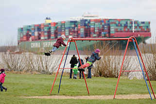 7674 Kinderspielplatz in Grnendeich an der Elbe - Kinder auf der Schaukel; im Hintergrund das havarierte Containerschiff CSCL Indian Ocean. 