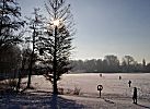 011_25889 | Spaziergnger gehen durch den verschneiten Stadtpark; der Stadtparksee ist zugefroren, ein Rettungsring hngt im Gegenlicht am Seeufer.