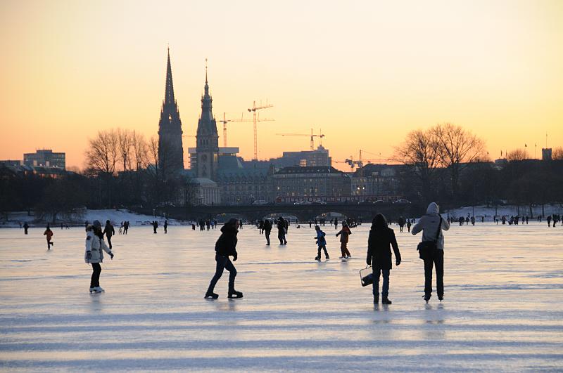 07_5925 |Alstereisvergngen auf dem Eis der zugefrorenen Auenalster. Im Abendlicht der untergehenden Sonne genieen die Hamburger auf dem Alster-Eis den Winter. Sie laufen Schlittschuh auf dem Eis des Hamburger Binnensees oder gehen einfach nur spazieren. Im Hintergrund fahren Autos und eine S-Bahn ber die Lombardsbrcken - neben den Baukrnen ragen die Trme der St. Nikolaikirche und des Hamburger Rathauses in den Abendhimmel.