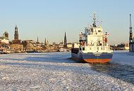 112_5837 | Ein Frachtschiff luft in den Hamburger Hafen ein - das Wasser der Elbe ist mit Treibeis bedeckt. Die Abendsonne scheint auf die Hamburger Silhouette mit den unterschiedlich hohen Trmen. Rechts ein Kran am Schwimmdock der Hamburger Werft Bohm + Voss.