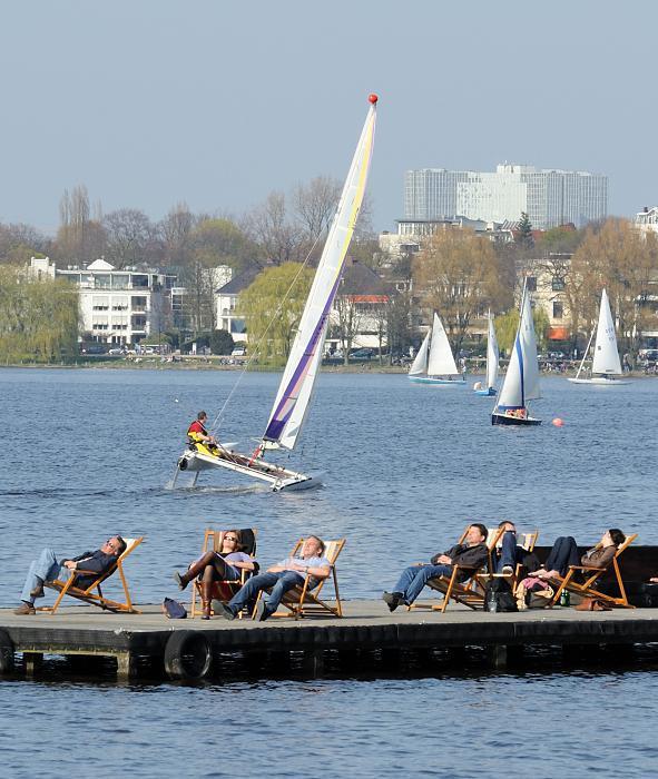 Frhling an der Alster! Segelboote und Sonnenhungrige im Liegestuhl. 118_2850 | Die Hamburger und Hamburgerinnen genieen die ersten Strahlen der Frhlingssonne in Liegesthlen auf einem Bootssteg an der Auenalster. Ein Katamaran und andere Segelboote segeln auf Hamburgs groen Binnensee. Die Weiden am Seeufer zeigen schon zartes Grn.