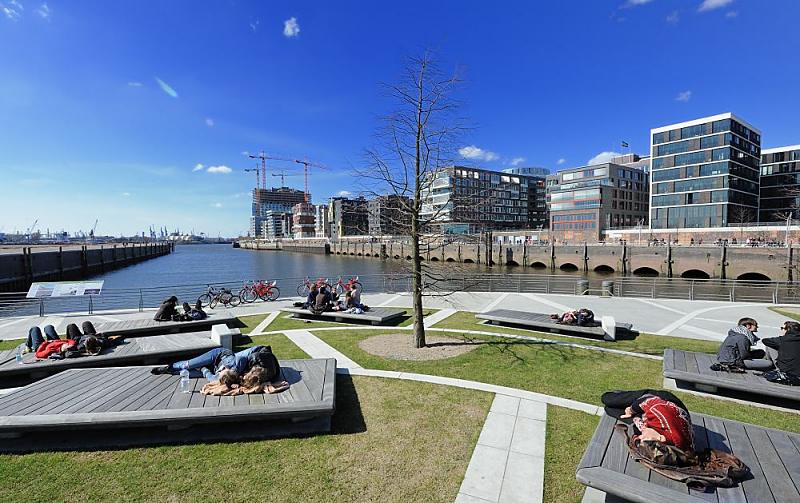 Frhling in der Hamburger Hafencity - sonnen auf den Marco Polo Terrassen. 121_1753 | Hamburger und Hamburgerinnen sonnen sich in der Frhlingssonne auf Holzbnken auf den Marco Polo Terrassen in der Hafencity - der Bau in der Mitte des Platzes zeigt noch keine Bltter. Im Hintergrund die Architektur am Dalmannkai des Grasbrookhafens.