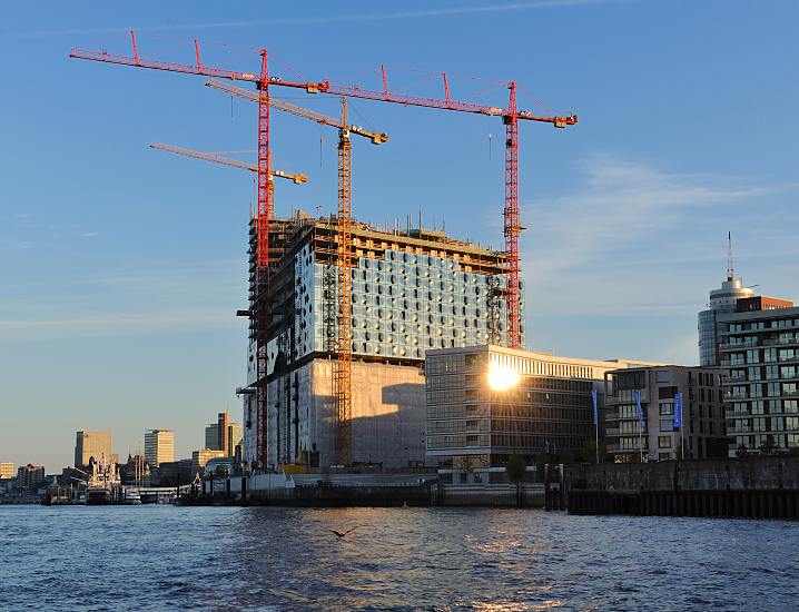 Hamburg am Morgen - Baustelle der Hamburger Elbphilharmonie in der Morgesonne.  125_4652 | Hamburg am frhen Morgen - die aufgehende Sonne spiegelt sich in einem der modernen Brogebude am Kai des Grasbrookhafens. Hohe Baukrne stehen auf der Grobaustelle der Elbphilharmonie. Im Hintergrund die berseebrcke mit dem Museumsschiff Cap San Diego und die Hochhuser von Hamburg St. Pauli. 