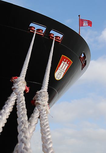 011_25990 | Kstarke Trossen halten das Contaienrschiff "Hanover" am Kai; am Bug trägt das neue Frachtschiff das Hamburger Wappen - eine Hamburg Flagge weht im Wind.