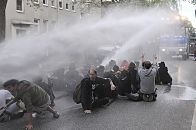 011_26020 |  Der Wasserwerfer versucht die Strassenblockierer aus zwei Rohren mit einem Wasserstrahl von der Strasse zu treiben. Zunchst halten die Demonstranten dem hohen Druck der Wasserkanone stand. 