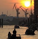 011_26040 |  Sonnenuntergang im Hamburger Hafen - die rote Abendsonne versinkt hinter den Hafenkrnen. Ein Sportboot / Motorboot, ein Festmacherboot und eine Barkasse fahren Richtung Elbe.  www.christoph-bellin.de 