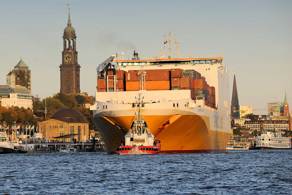 7520 Das RoRo Frachtschiff Grande Angola verlsst den Hambuger Hafen; mit Hilfe von Schleppern wird der Frachter in die Fahrrinne geschleppt. Links vom Schiff die Kuppel vom alten Elbtunnel und der Kirchturm der St. Michaeliskirche - re. Fahrgastschiffe an den St. Pauli Landungsbrcken.