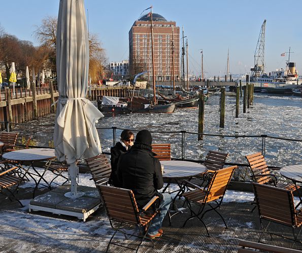 41_656544 | Die Cafes am Elbufer in Hamburg Oevelgnne sind bei hufig auch im Winter geffnet - so ist es mglich in der Wintersonne am Museumshafen von Hamburg Oevelgoenne zu sitzen und auf das Eis der Elbe zu blicken. Im Hintergrund das ehemalige Khlhaus von Hamburg Neumhlen, in dem jetzt Senioren leben, die in der Lage sind ab ca. 2000 EUR monatlich zu zahlen. www.fotograf-hamburg.de