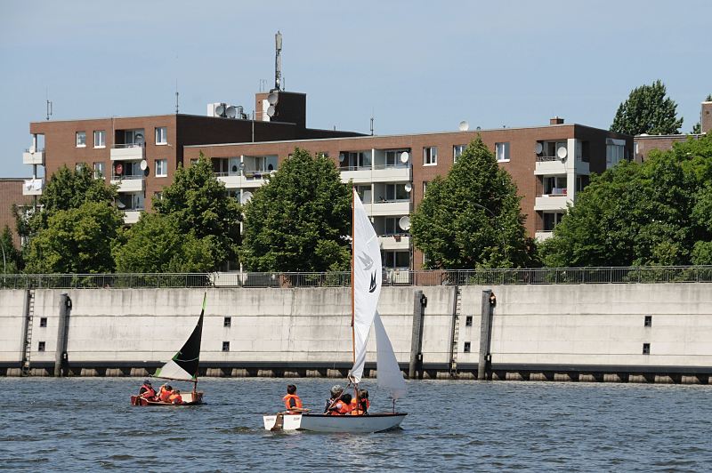 93-9604 |Bilder aus aus den Hamburger Stadtteilen - Schler und Schlerinnen der Schule Slomanstieg knnen auf dem Wasser des Mggenburger Zollhafens das Segeln lernen. Die Kinder sitzen in den Optimistenjollen und tragen signalrote Schwimmwesten - am Ufer des Hafens ein Wohngebude der Veddel. www.fotograf- hamburg.de