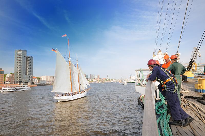 4450_3175 | Segelschiff vor Hamburg Altona zur Einlaufparade des Hamburger Hafengeburtstages. Matrosen blicken von Bord ihres Schiffs auf die Elbe. Der Grosssegler berholt gerade ein kleineres Segelschiff - im Hintergrund ein Ausflugsschiff vor der modernen Architektur an der Grossen Elbstrasse. Der Hamburger Hafengeburtstag ist das grte Hafenfest der Welt; mehr als 1,5 Mio. Gste aus aller Welt besuchen den Geburtstag des Hamburger Hafens. Viele Grosssegler und Traditionsschiffe beteiligten sich an der traditionellen Schiffsparade auf der Elbe vor den Landungsbrcken bis hinauf nach Wedel.  