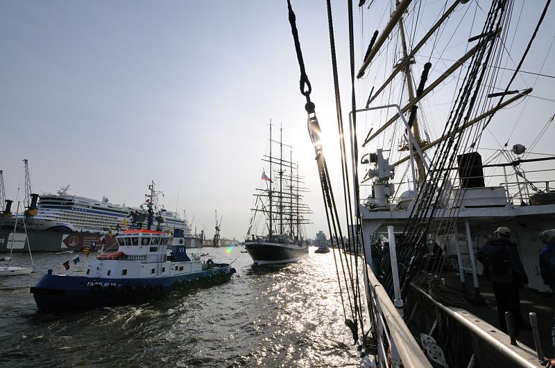 5050_3203 | Nach der Einlaufparade wird einer der grossen russischen Segelschiffe mit Hilfe eines Hafenschleppers zu seinem Liegeplatz an den Landungsbrcken gebracht. Im Hintergrund ein modernes Kreuzfahrtschiff im Dock der Werft Blohm + Voss. Der Hamburger Hafengeburtstag ist das grte Hafenfest der Welt; mehr als 1,5 Mio. Gste aus aller Welt besuchen den Geburtstag des Hamburger Hafens. Viele Grosssegler und Traditionsschiffe beteiligten sich an der traditionellen Schiffsparade auf der Elbe vor den Landungsbrcken bis hinauf nach Wedel.