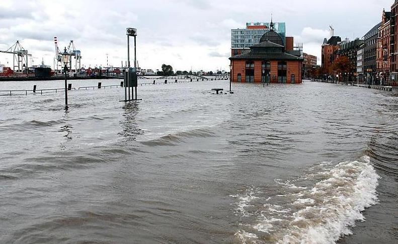 387_7344 Sturmflut in Hamburg, das Wasser tritt ber die Kaimauern und bersplt den Altonaer Fischmarkt und die Groe Elbstrasse. Die vielbefahrene Strasse am Hafenrand ist fr den Strassenverkehr gesperrt. Die Fischauktionshallte ist vom Hochwasser berflutet, die Wassertreppe zum Fhranleger Fischmarkt Altona steht fast unter Wasser - der Fhrverkehr ist hier eingestellt. Am gegenber liegenden Ufer die Containeranlagen des HHLA Terminals Tollerort.