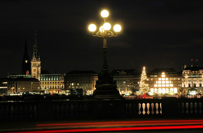 089_1277 Nachtaufnahme von der Lombardsbrcke - Blick auf die Hamburger Innenstadt, Weihnachtsbaum. Lombardsbrcke bei Nacht - die Rcklichter fahrender Autos hinterlassen bei der Langzeitaufnhambe rote Lichtstreifen. Die historische Kandelaber auf der historischen Hamburger Brcke ist mit leuchtenden Kugelglsern versehen. Im Hintergrund auf der Binnenalster die Weihnachtstanne / Alstertanne - die Geschfte und Kaufhuser am Jungfernstieg sind hell erleuchtet; lks. das Gebude des Hamburger Rathauses, auf dem Rathausmarkt findet ein groer Weihnachtsmarkt statt. 