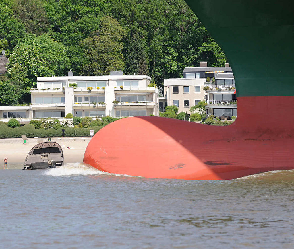 8886 Wulstbug vom Containerfrachter Thalassa Axia auf der Elbe vor Hamburg Blankenese; am Strand ein altes Schiffswrack. Der Containerfrachter wurde 2014 gebaut und kann 13 808 TEU Standardcontainer transportieren.