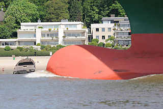 8886 Wulstbug vom Containerfrachter Thalassa Axia auf der Elbe vor Hamburg Blankenese; am Strand ein altes Schiffswrack. Der Containerfrachter wurde 2014 gebaut und kann 13 808 TEU Standardcontainer transportieren. 