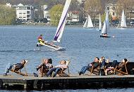 118_2850 | Die Hamburger und Hamburgerinnen genieen die ersten Strahlen der Frhlingssonne in Liegesthlen auf einem Bootssteg an der Auenalster. Ein Katamaran und andere Segelboote segeln auf Hamburgs groen Binnensee. Die Weiden am Seeufer zeigen schon zartes Grn.