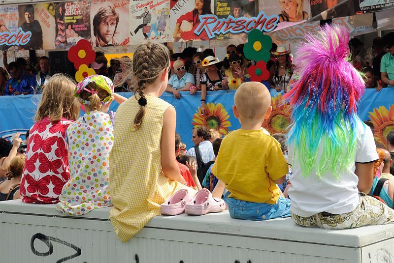 Schlagermove Hamburg - Truckparade an den St. Pauli Landungsbrcken / Kinder. 129_9833 | Kinder sehen dem bunten Treiben auf dem Schlagermove zu - ein mit Sonnenblumen und Plattencovern der 70er Jahre dekorierter Truck fhrt gerade vorbei. 44 geschmckte Lastwagen fahren auf der Parade des Hamburger Schlagermoves mit -  ca. 500 000 im Stil der 1970er Jahre verkleidete Besucher und Besucherinnen sumen die Strecke des Konvois oder begleiten die Fahrzeug, die nach dem Motto "Ein Festival der Liebe" dekoriert sind. Laute Schlagermusik zum Mitsingen kommt aus den Lautsprechern der Lastwagen.bilder-hamburg.de