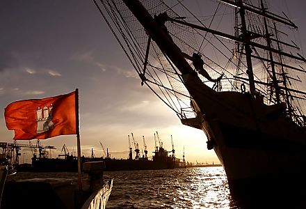 011_25991 |  Sonnenuntergang im Hamburger Hafen; an den St. Pauli Landungsbrcken liegt ein Grosssegler - im Hintergrund am gegenber liegenden Elbufer die Werft Blohm + Voss, rechts weht die Hamburg Fahne im Wind.