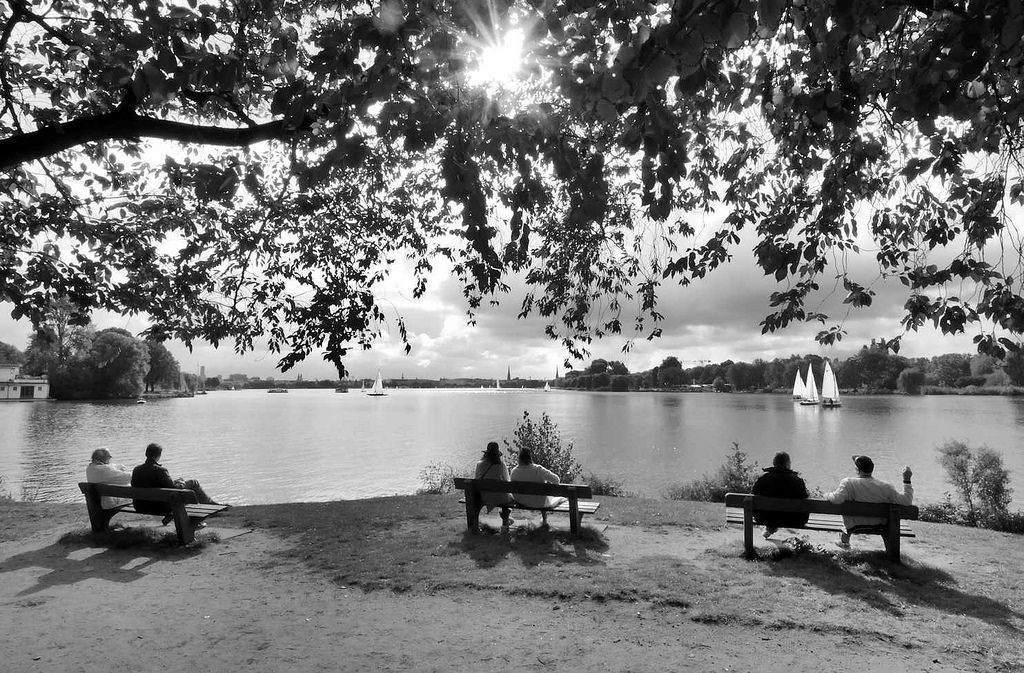 0015 Sonnentag an der Hamburger Aussenalster - einige Segelboote sind auf dem Wasser; HamburgerInnen sitzen auf Holzbnken und blicken auf die Alster.