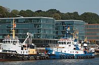 011_26032 | Die Schlepper WILHELMINE und FAIRPLY VI liegen an Anleger Neumhlen und warten auf grosse Frachtschiffe, die von den PS-starken Arbeitsbooten an ihren Liegeplatz im Hamburger Hafen gebracht werde. Die Schlepper sind mit einer dichten Reihe von Autoreifen bestckt, die das Schiff beim Bugsieren schtzen sollen. Im Hintergrund Hamburgs neue Architektur in Neumhlen am Elbufer - die sogen. architektonische Perlenkette an der  Neumhlen Kaistrasse ist zum Wasser hin hochstehend, damit der untere Bereich der Brogebude vor Hochwasser der Elbe geschtzt sind. Im Hintergrund Bume an der Elbtreppe. www.christoph-bellin.de