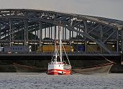 011_26043 |  Ein rotes Finkenwerder Fischereiboot fischt vor den Hamburger Elbbrcken - lks. und re. des Fischerboots sind die Netze zu erkennen, die in das Elbwasser gesenkt werden. Auf den Elbbrcken ist ein Stau - Lastwagen stehen dicht an dicht zwischen dem Brckenbogen und Brckenpfeilern aus Eisen.   www.christoph-bellin.de 