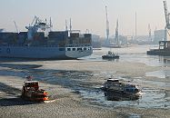 41_656541 |  Eisgang auf der Elbe - Hafenfhren bahnen sich ihren Weg durch die Eisschollen auf dem Wasser im Hamburger Hafen. Ein Containerriese ist in den Hafen eingelaufen und wird von einem Schlepper rckwrts zu seinem Liegeplatz am Container Terminal Tollerort gezogen. Die Ausleger der Hafenkrane stecken sich in den dunstigen Winterhimmel Hamburgs.  www.fotograf-hamburg.de