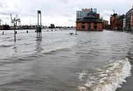 387_7344 Sturmflut in Hamburg, das Wasser tritt ber die Kaimauern und bersplt den Altonaer Fischmarkt und die Groe Elbstrasse. Die vielbefahrene Strasse am Hafenrand ist fr den Strassenverkehr gesperrt. Die Fischauktionshallte ist vom Hochwasser berflutet, die Wassertreppe zum Fhranleger Fischmarkt Altona steht fast unter Wasser - der Fhrverkehr ist hier eingestellt. Am gegenber liegenden Ufer die Containeranlagen des HHLA Terminals Tollerort.