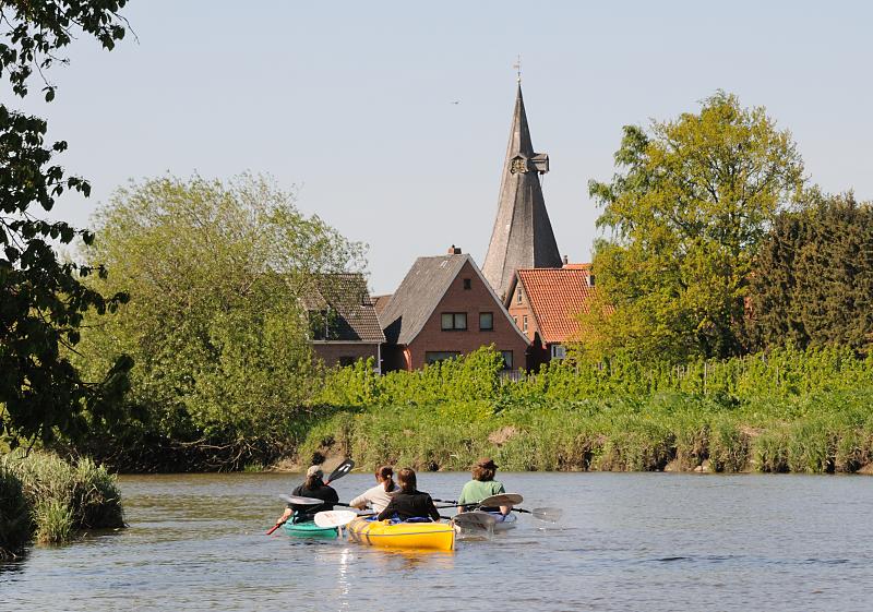 10000_2529 | Kanuten auf dem Lauf der Este bei Estebrggee - hinter der Obstplantage Huser des Orte und der Kirchturm der St. Maritinikirche an der Este. Die 44,7 km lange Este ist ein linker Nebenfluss der Elbe in Niedersachsen und Hamburg - Die untere Este ist von der Mndung bis zum Unterwasser der Schleuse am Buxtehuder Hafen eine Bundeswasserstrae der Klasse I, auf der die Seeschifffahrtsstraen-Ordnung gilt. Bis in die erste Hlfte des 20. Jahrhunderts wurde die Este als Transportweg fr Lastkhne und Schuten genutzt. 