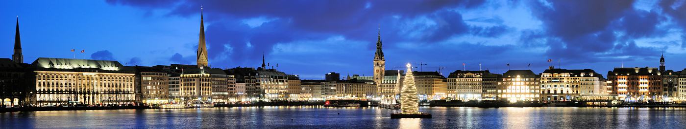 023_1294_98 Blaue Stunde ber der Hamburger Binnenalster - Abenddmmerung in der Hamburger Innenstadt. Die Geschftshuser / Kontorhuser am Ballindamm und Jungfernstieg sind beleuchtet; im Bildzentrum die Altertanne, die zu Weihnachten mit Lichterketten geschmckt auf einem Ponton in der Binnenalster schwimmt und der Hansestadt eine weihnachtliche Atmosphre vermitteln. Abendliches Panorama - Nachtaufnahme der Gebude am Ufer der Binnenalster - Kirchtrme Hamburgs; hinter den beleuchteten Tannenbumen der Turm des Hamburger Rathauses, ganz rechts der Kuppelturm der Hamburger Michaeliskirche.