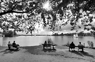 0015 Sonnentag an der Hamburger Aussenalster - einige Segelboote sind auf dem Wasser; HamburgerInnen sitzen auf Holzbnken und blicken auf die Alster.