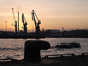 011_25894 | Abenddmmerung an der Elbe; Eisenpoller am Kai, eine Barkasse der Hafenrundfahrt fhrt an ihren Liegeplatz - im Hintergrund der rotgefrbte Abendhimmel und die Silhouetten der Krne.